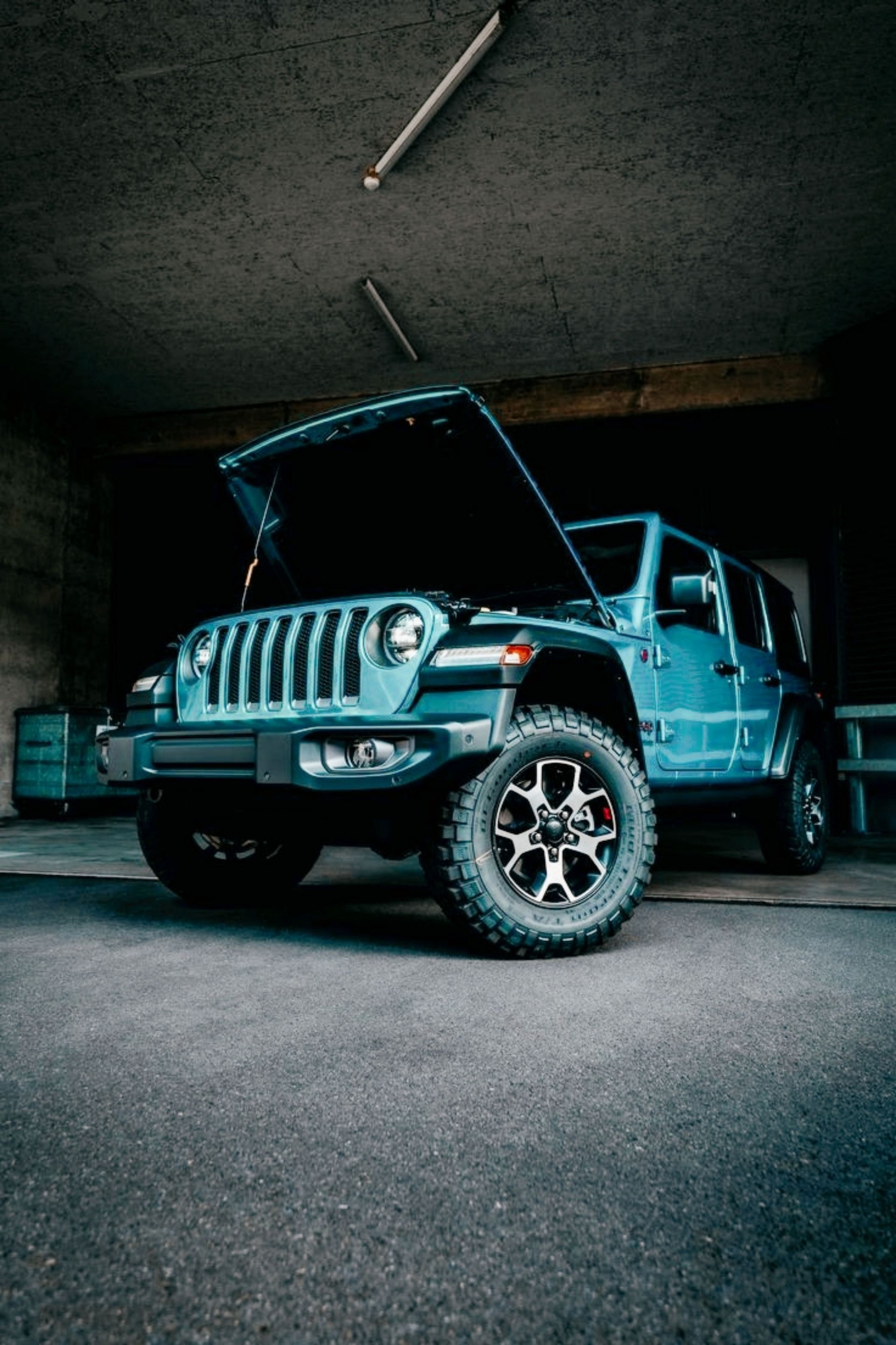 A rugged blue SUV with open hood parked inside a dimly lit garage, showcasing its off-road capabilities.